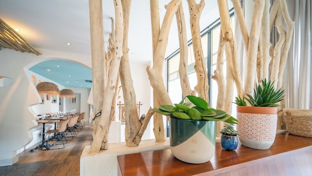 A reception area with a wooden reception desk, potted plants, and a view of the dining area. - La Finca Hôtel & Spa (Paris)