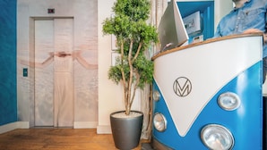 A blue vintage car-shaped reception desk with a logo, a potted plant, and an elevator in the background. - La Finca Hôtel & Spa (Paris)
