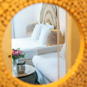 A bed with white bedding, a small round table with a vase of flowers, and a bottle of champagne.