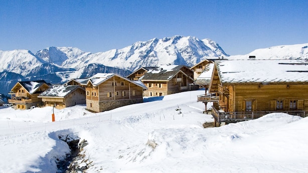 A row of wooden cabins with a snowy mountain backdrop. - Madame Vacances Les Chalets de l'Altiport (Huez)