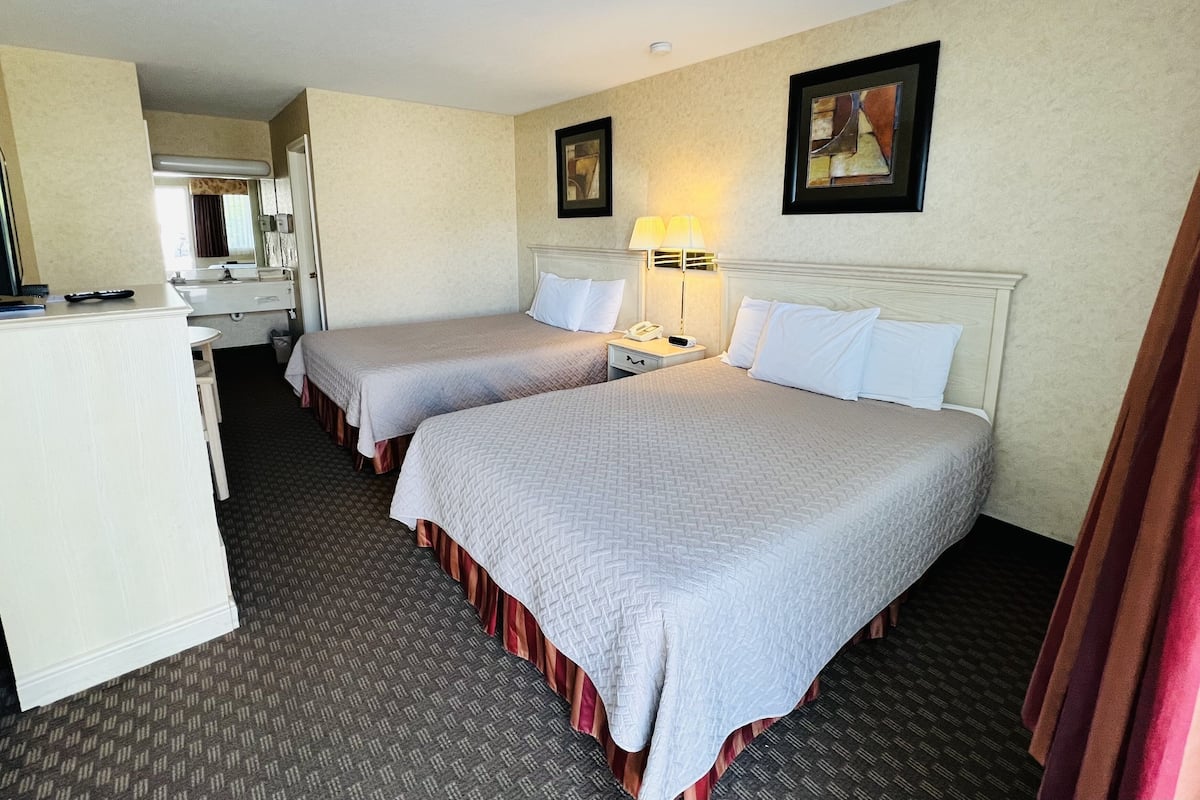 A hotel room with two beds, a desk, a mirror, and a nightstand with a lamp.
