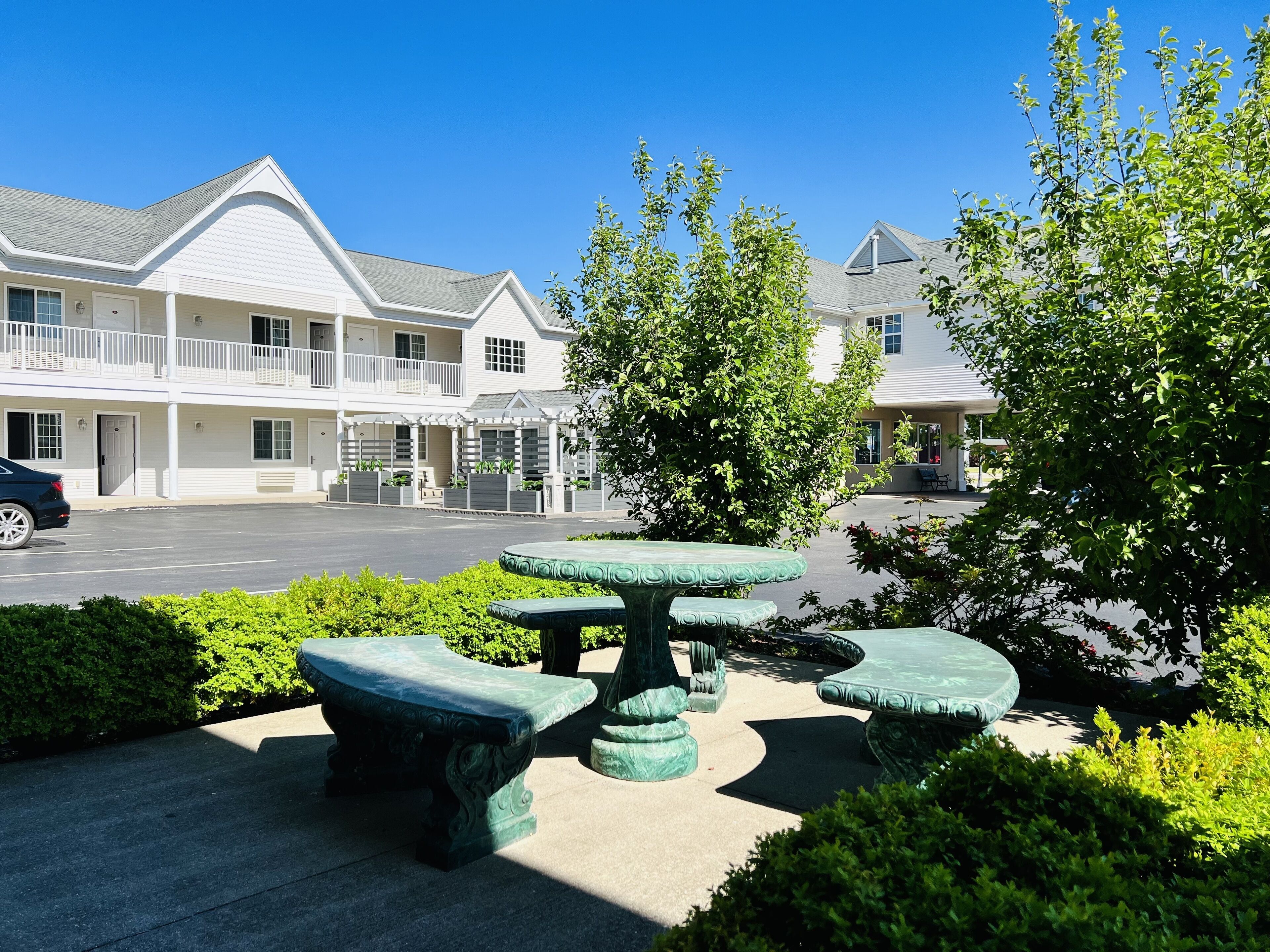 A courtyard with a stone table and benches, surrounded by greenery and a building with a balcony.