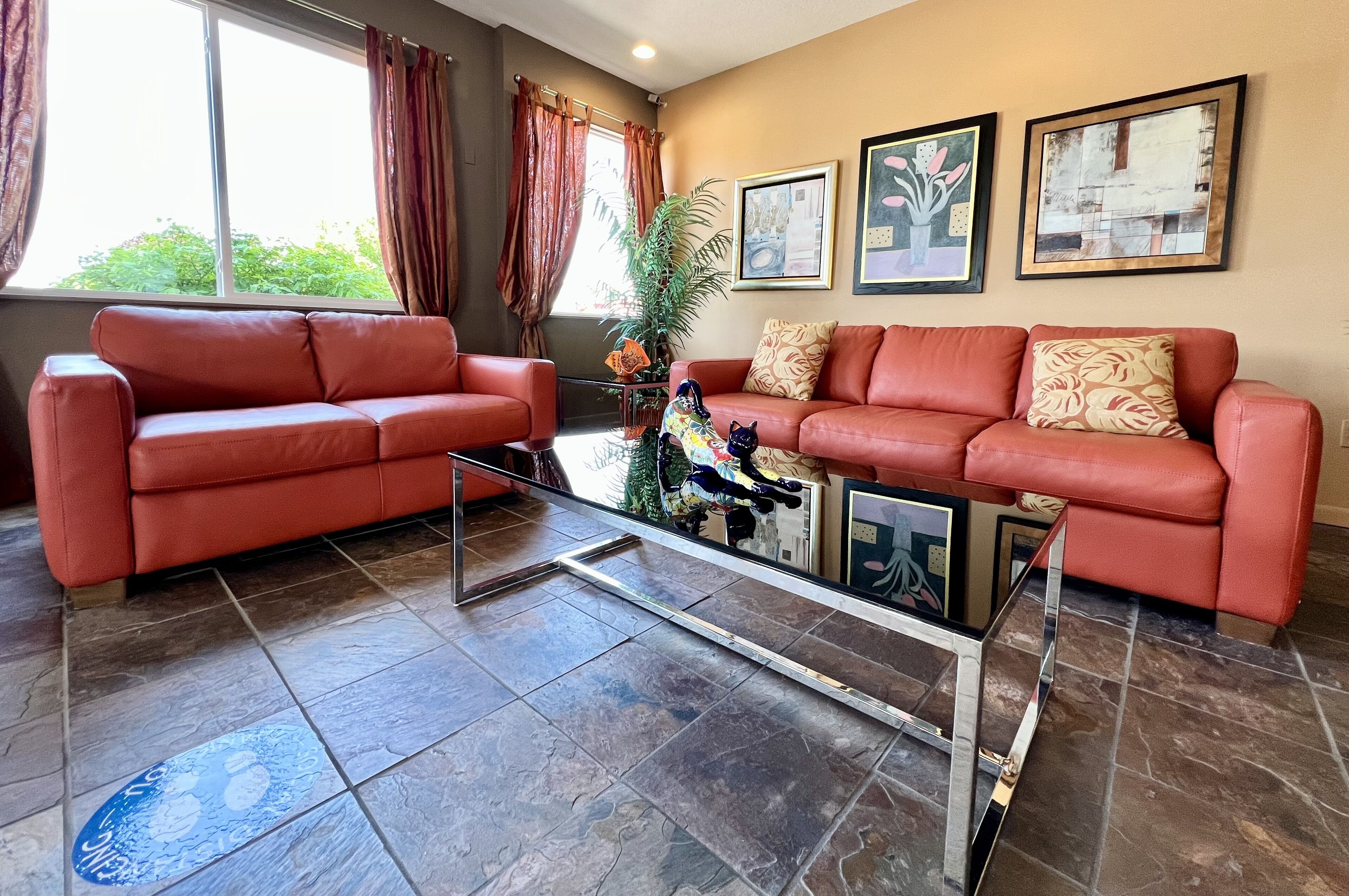 A living room with two red leather sofas, a glass coffee table, and a large window with curtains.