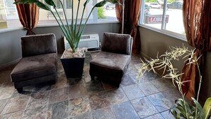 A lobby with two dark brown sofas, a large potted plant, and a floor lamp. - Court Plaza Inn & Suites (Mackinaw City)