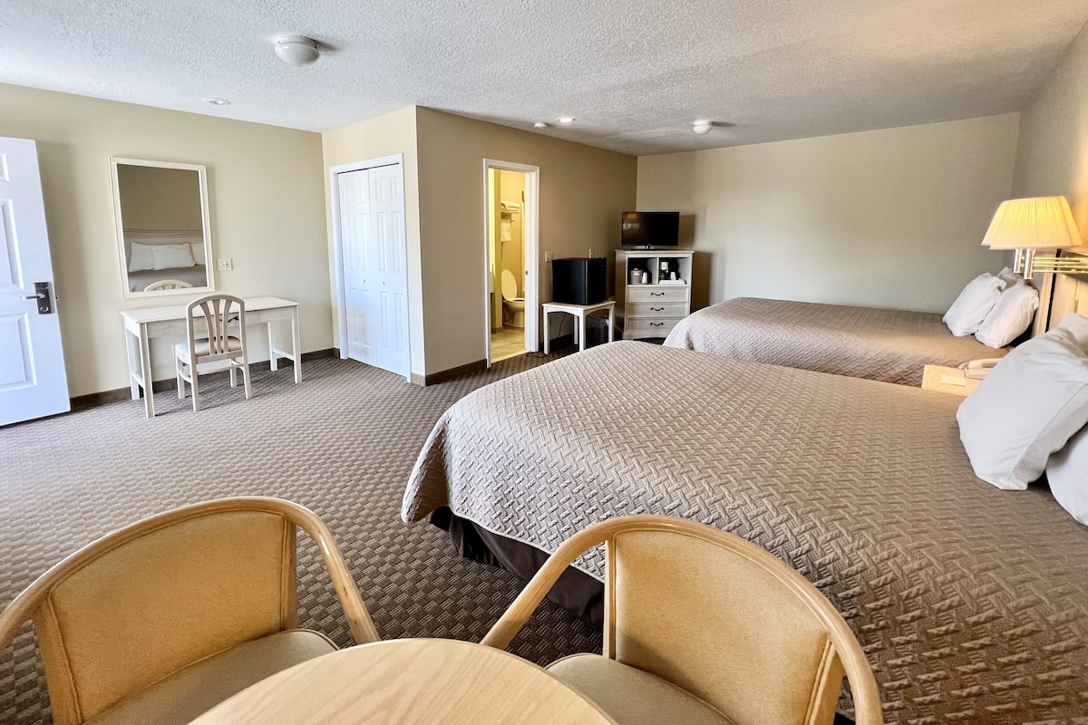 A hotel room with two beds, a desk, a chair, a television, and a lamp.