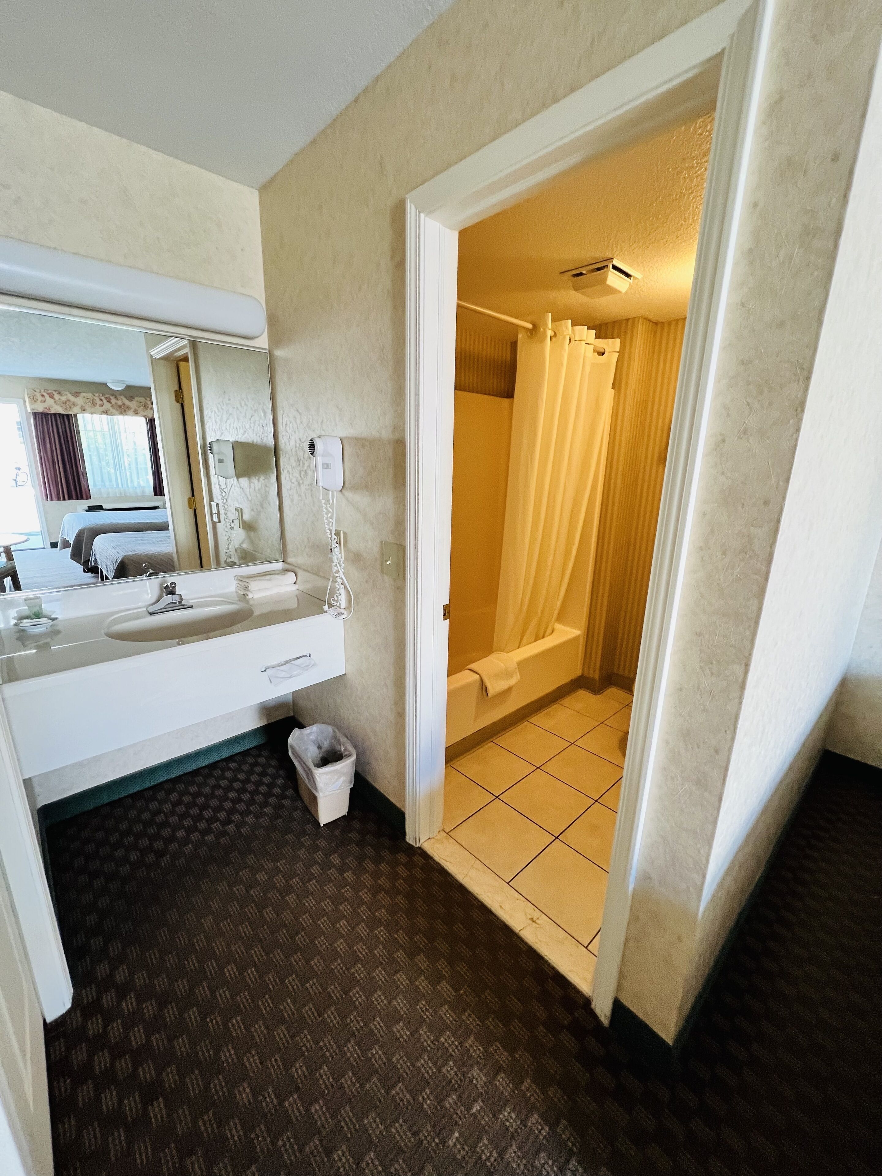 Un baño de hotel con un espejo grande, un lavabo, un inodoro y una zona de ducha.