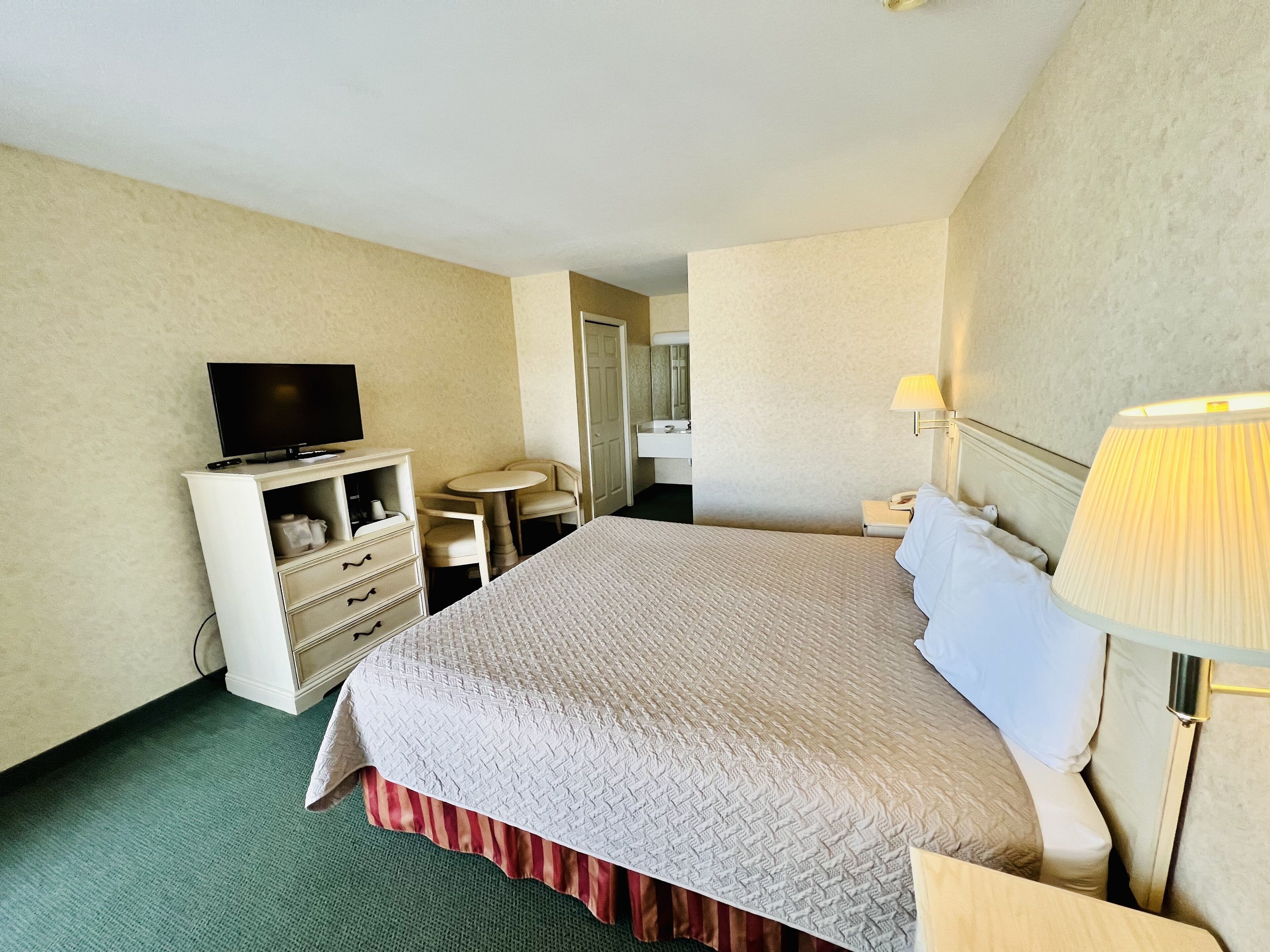 A hotel room with a bed, a TV, a desk, a chair, a lamp, and a mirror.