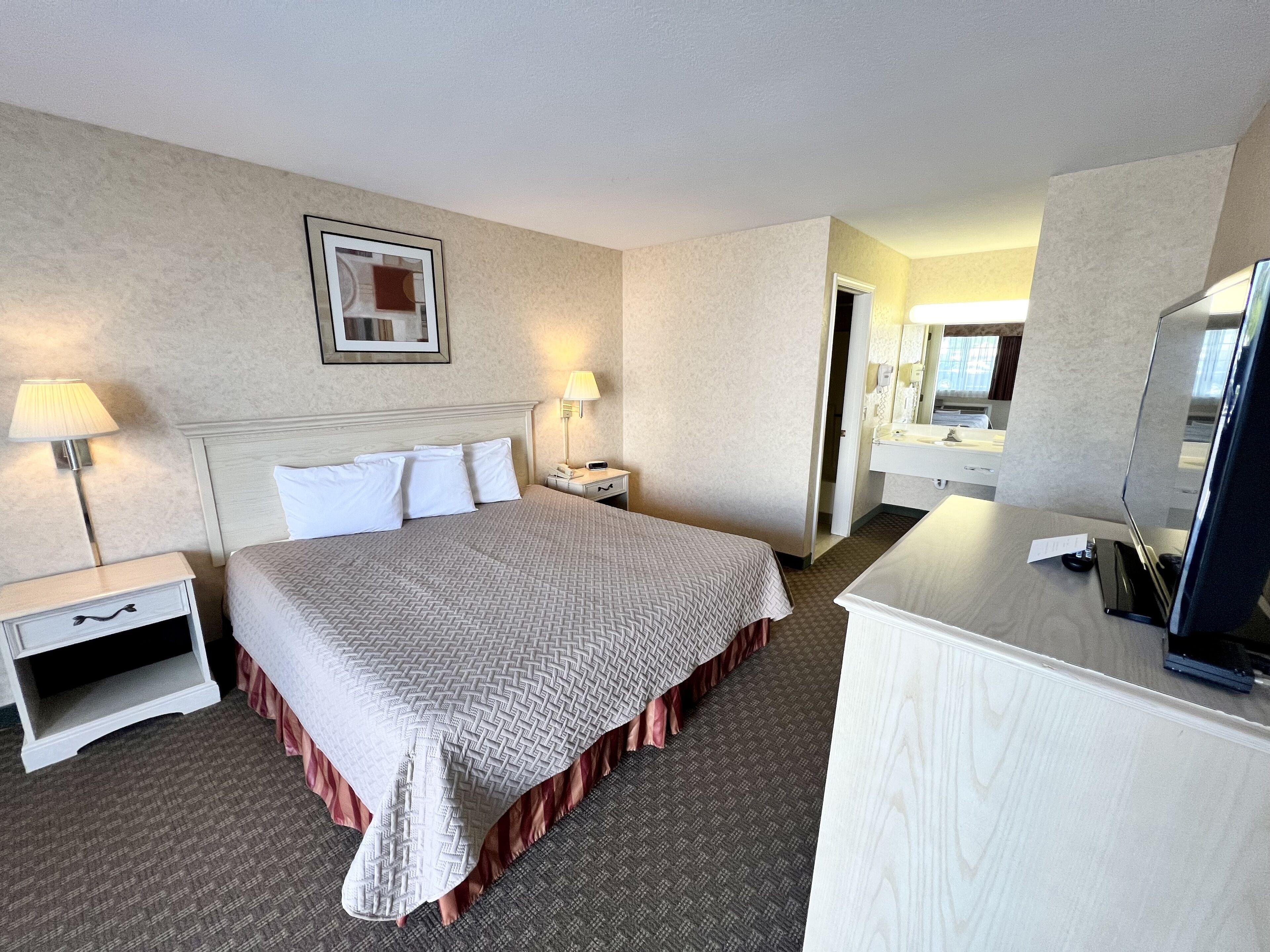 Habitación de hotel con cama, mesitas de noche con lámparas, escritorio con computadora y espejo.