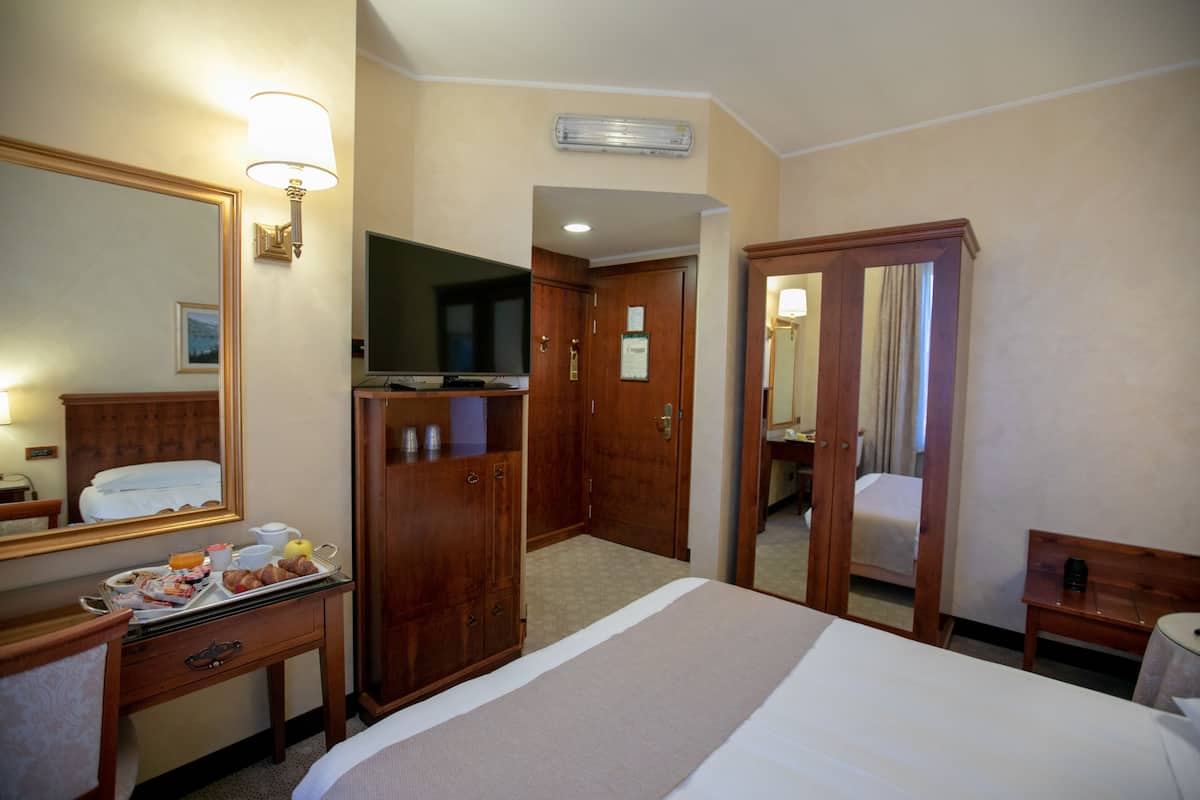 Una habitación de hotel con una cama, un escritorio con una bandeja de desayuno, un televisor y un espejo.