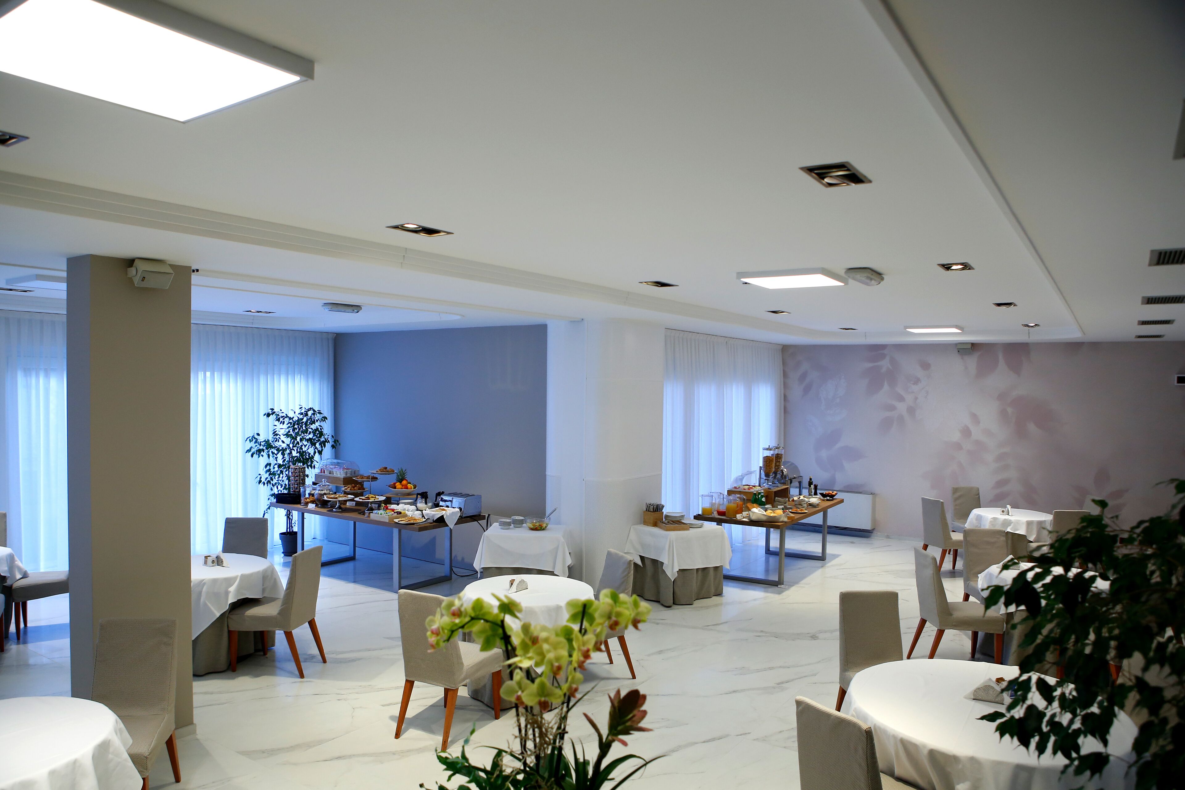 A hotel dining area with round tables, chairs, and a buffet setup.
