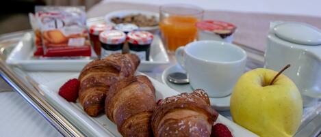 A breakfast tray with croissants, raspberries, a pear, and a cup of coffee on a hotel room table.