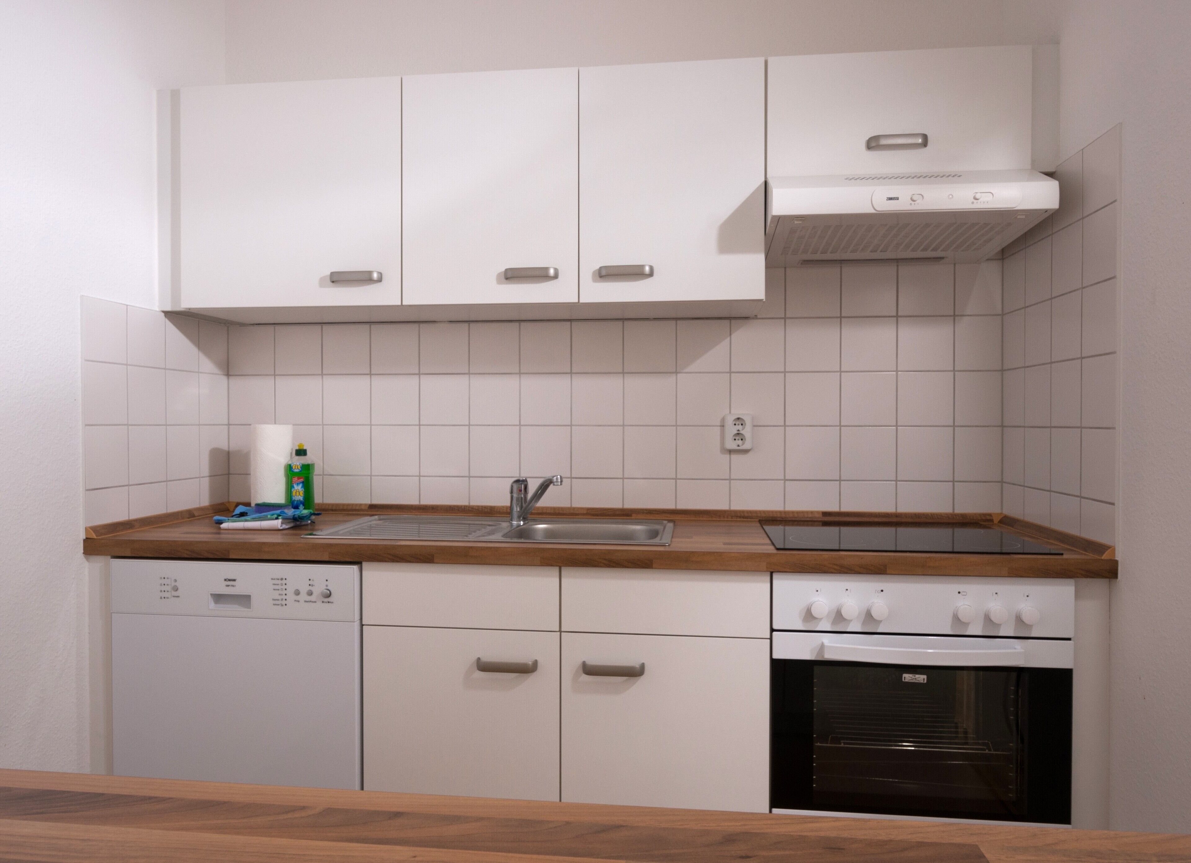 A compact kitchen with white cabinets, a wooden countertop, a built-in dishwasher, and an oven.
