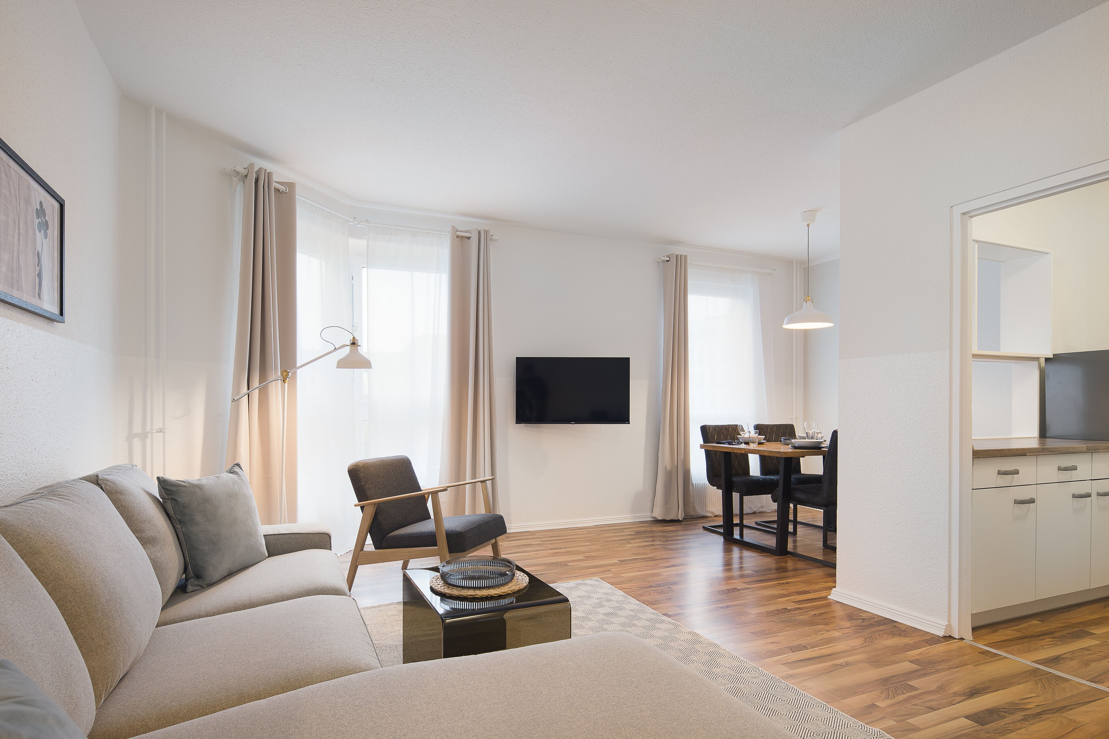 Una sala de estar moderna con un sofá, un comedor con una mesa y sillas, y una cocina con armarios y encimera.