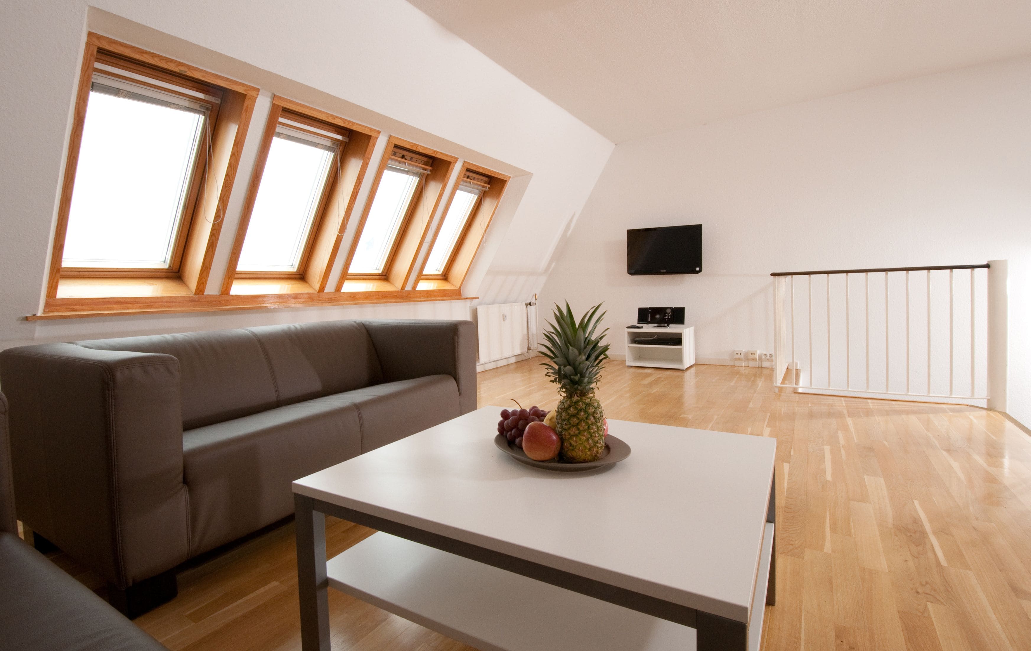 Un salon moderne avec un canapé, une table sur laquelle se trouvent des fruits, un téléviseur et un escalier.
