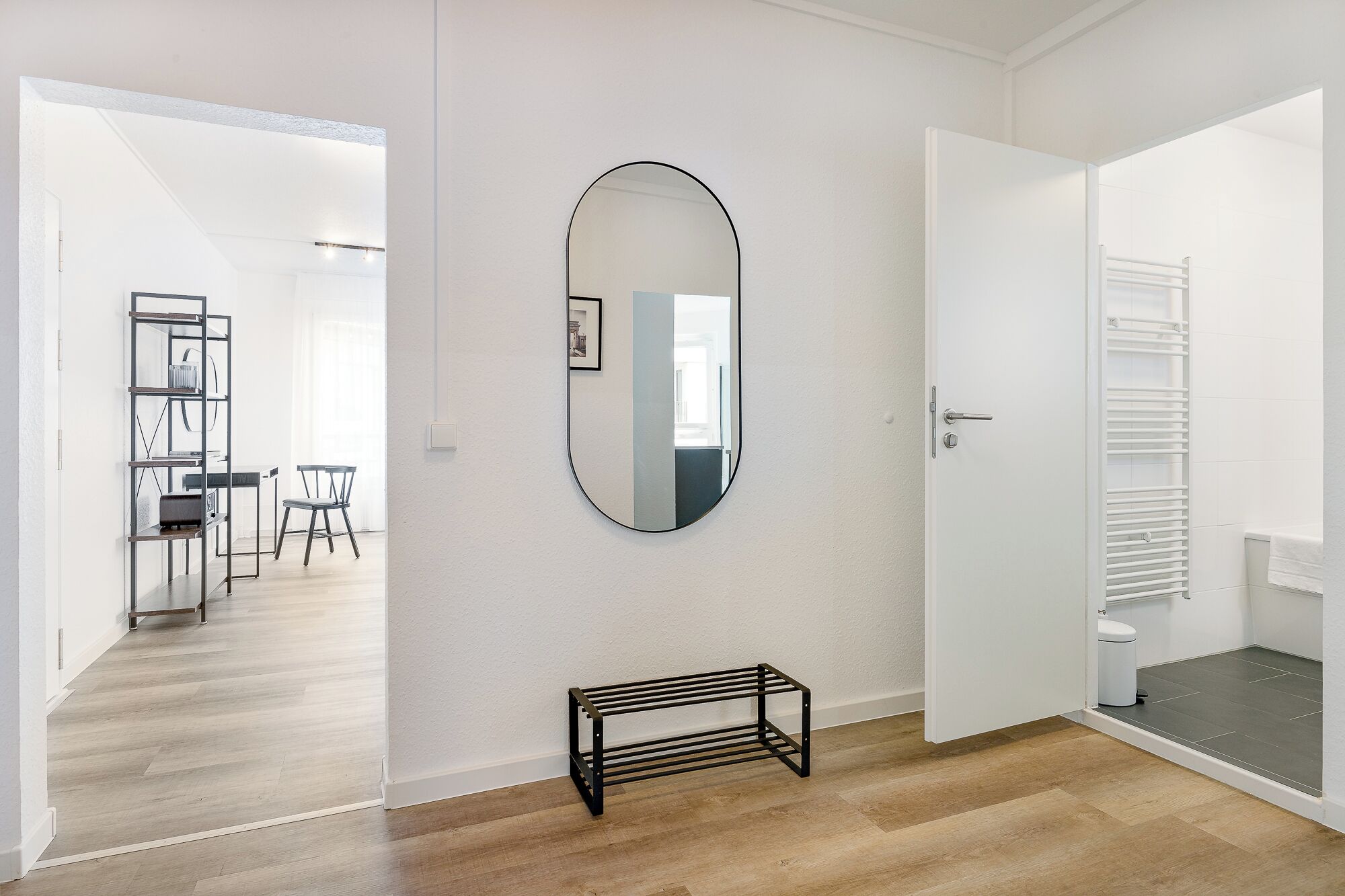 Un interior moderno con piso de madera, una estantería de metal negro y un espejo grande en la pared.