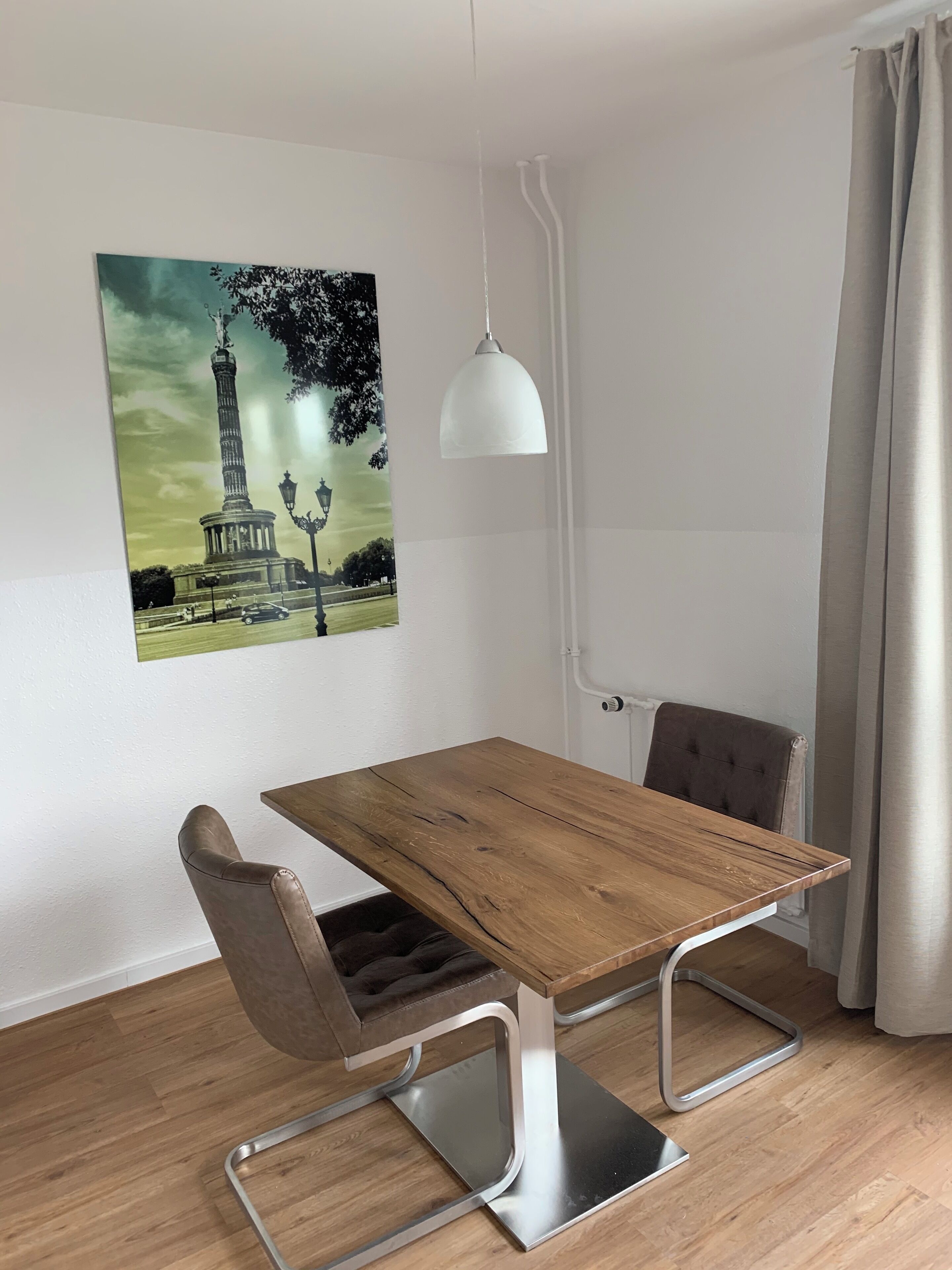 A dining area with a wooden table, a single chair, a pendant light, and a wall-mounted picture of a monument.