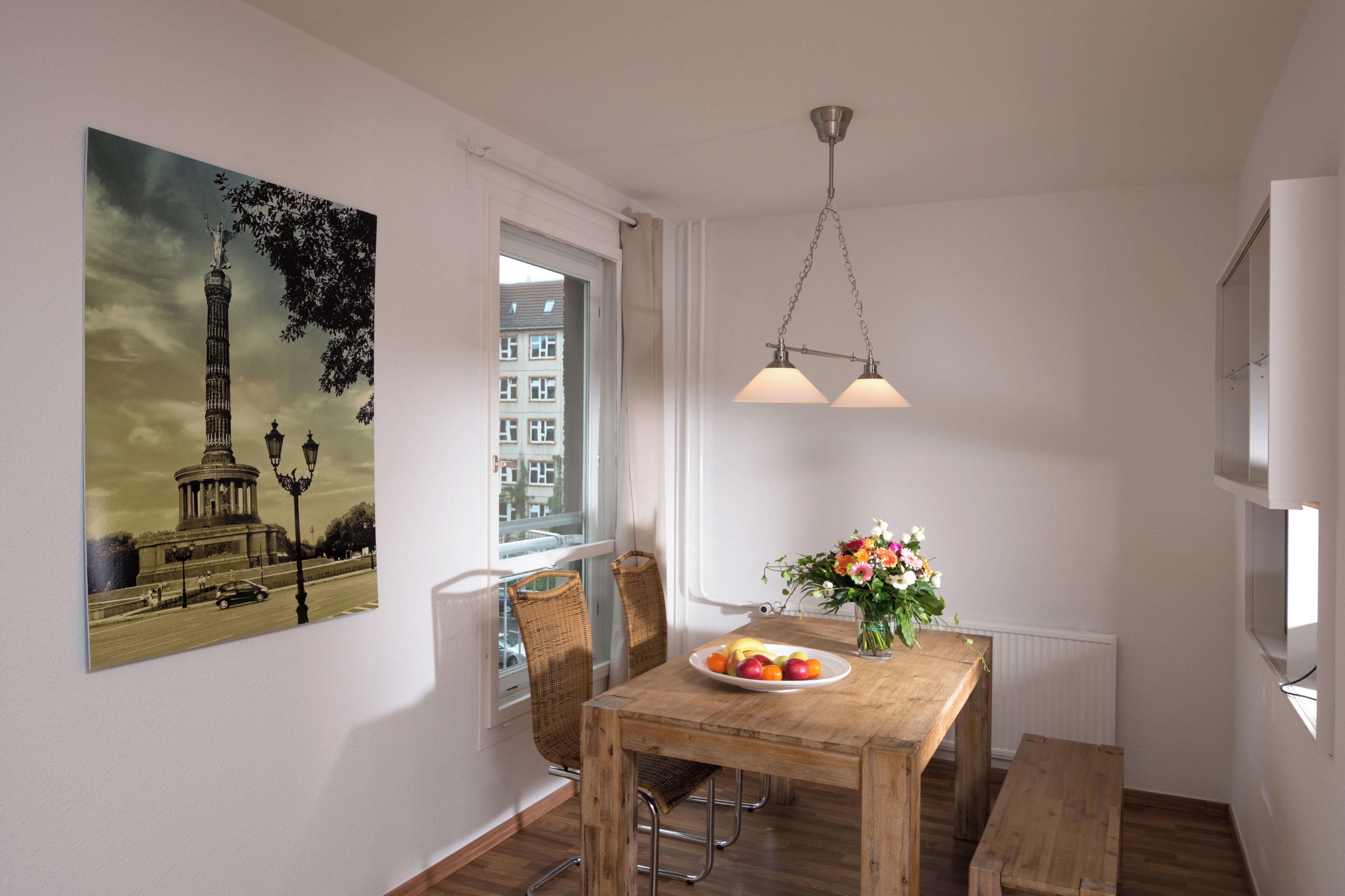 Un comedor con una mesa de madera, sillas, un jarrón con flores y un cuadro de una torre en la pared.