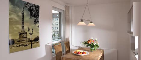 Un comedor con una mesa de madera, sillas, un jarrón con flores y un cuadro de una torre en la pared.