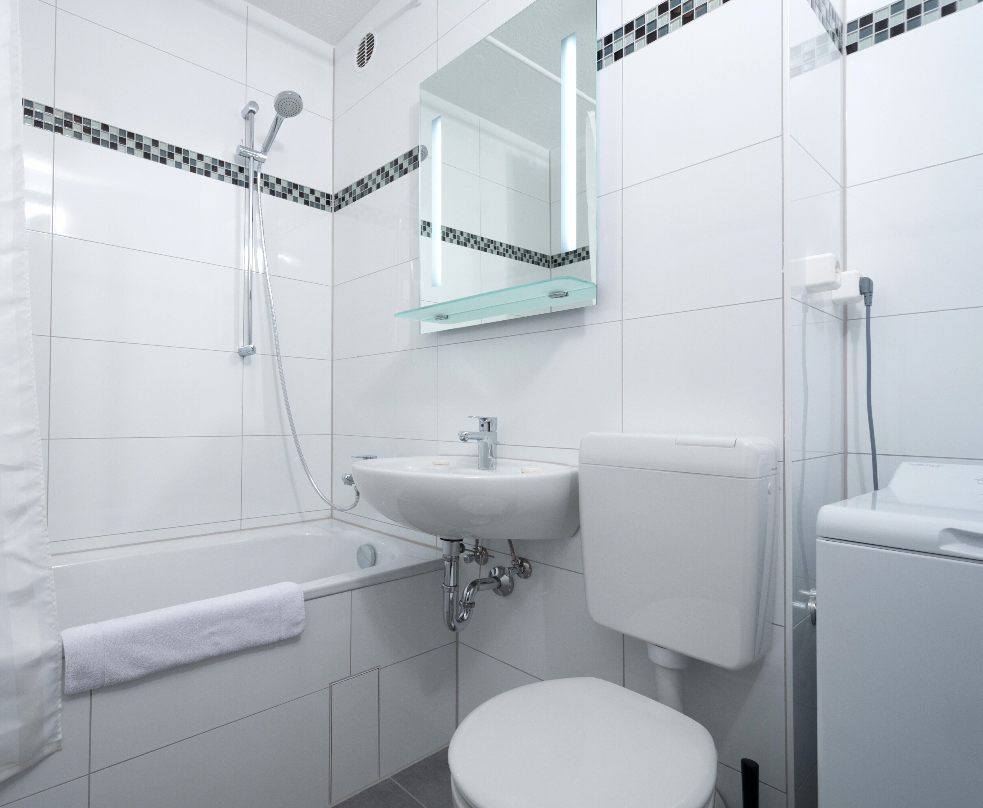 Een moderne badkamer met een bad, een wastafel, een toilet en een glazen plank boven de wastafel.