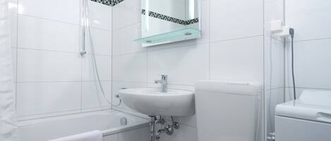 Een moderne badkamer met een bad, een wastafel, een toilet en een glazen plank boven de wastafel.