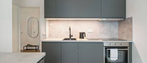A modern kitchen with grey cabinets, a built-in oven, and a stainless steel range hood.