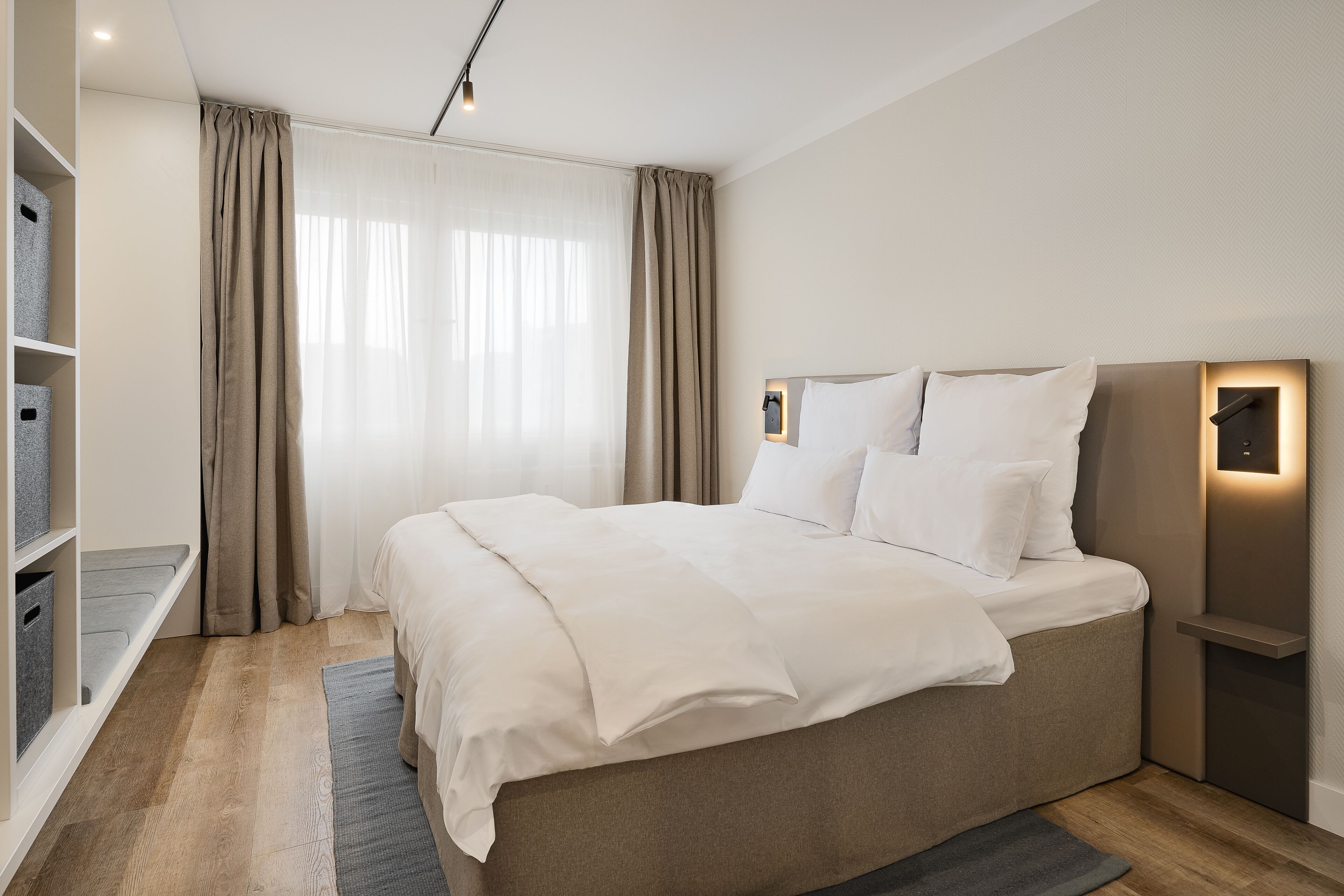 A modern bedroom with a large bed, built-in shelving, and a bedside table with a lamp.