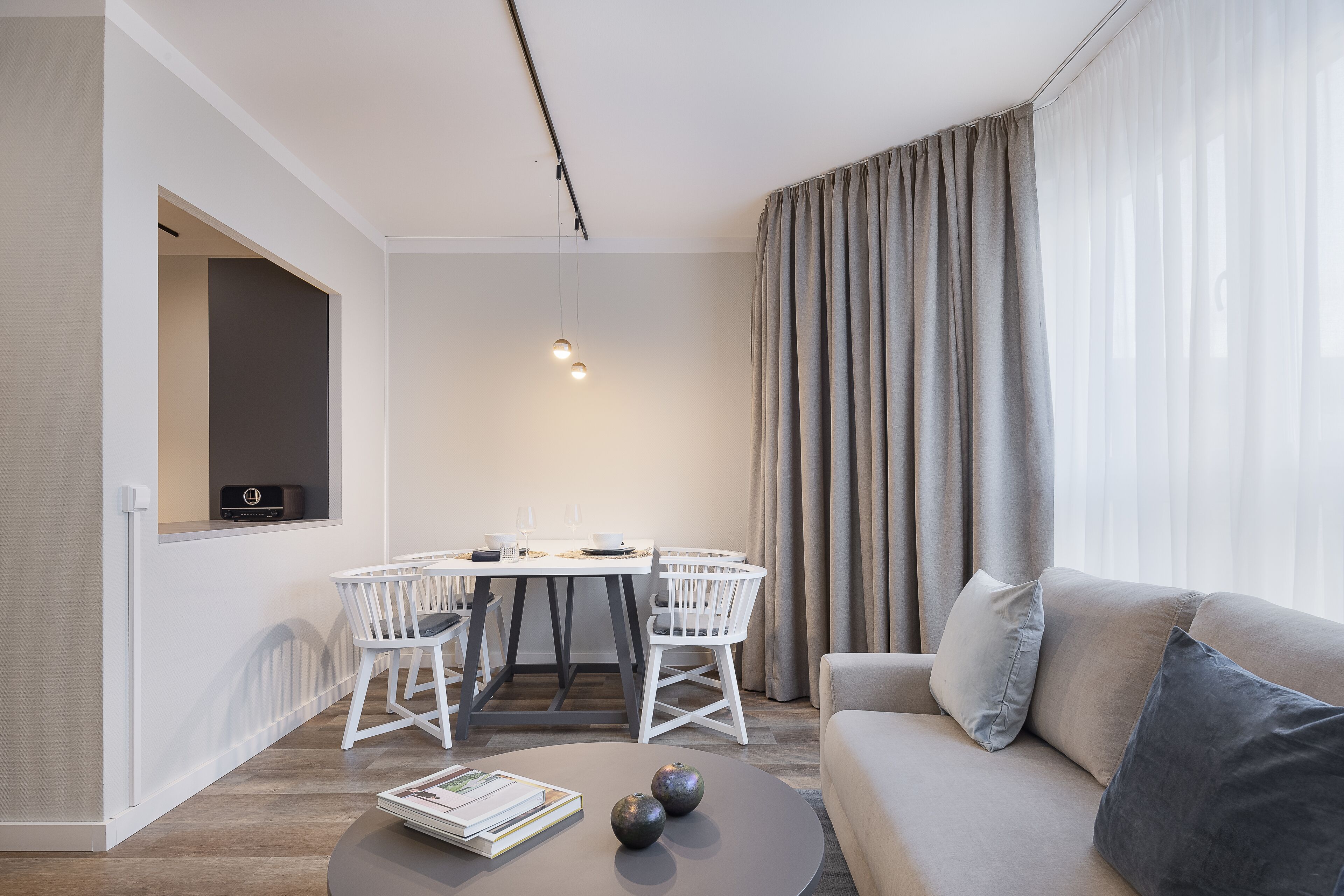 A modern living room with a sofa, a dining table with chairs, and a TV mounted on the wall.