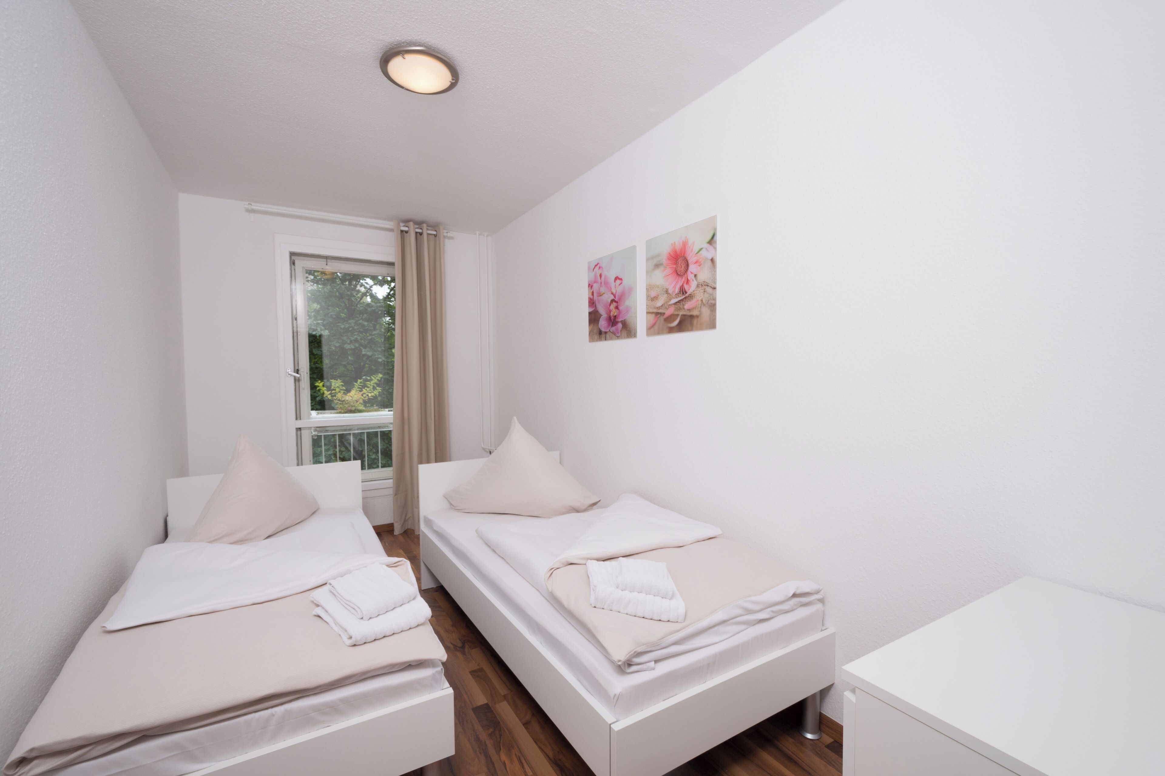 A room with two single beds, a small white desk, and a window with curtains.