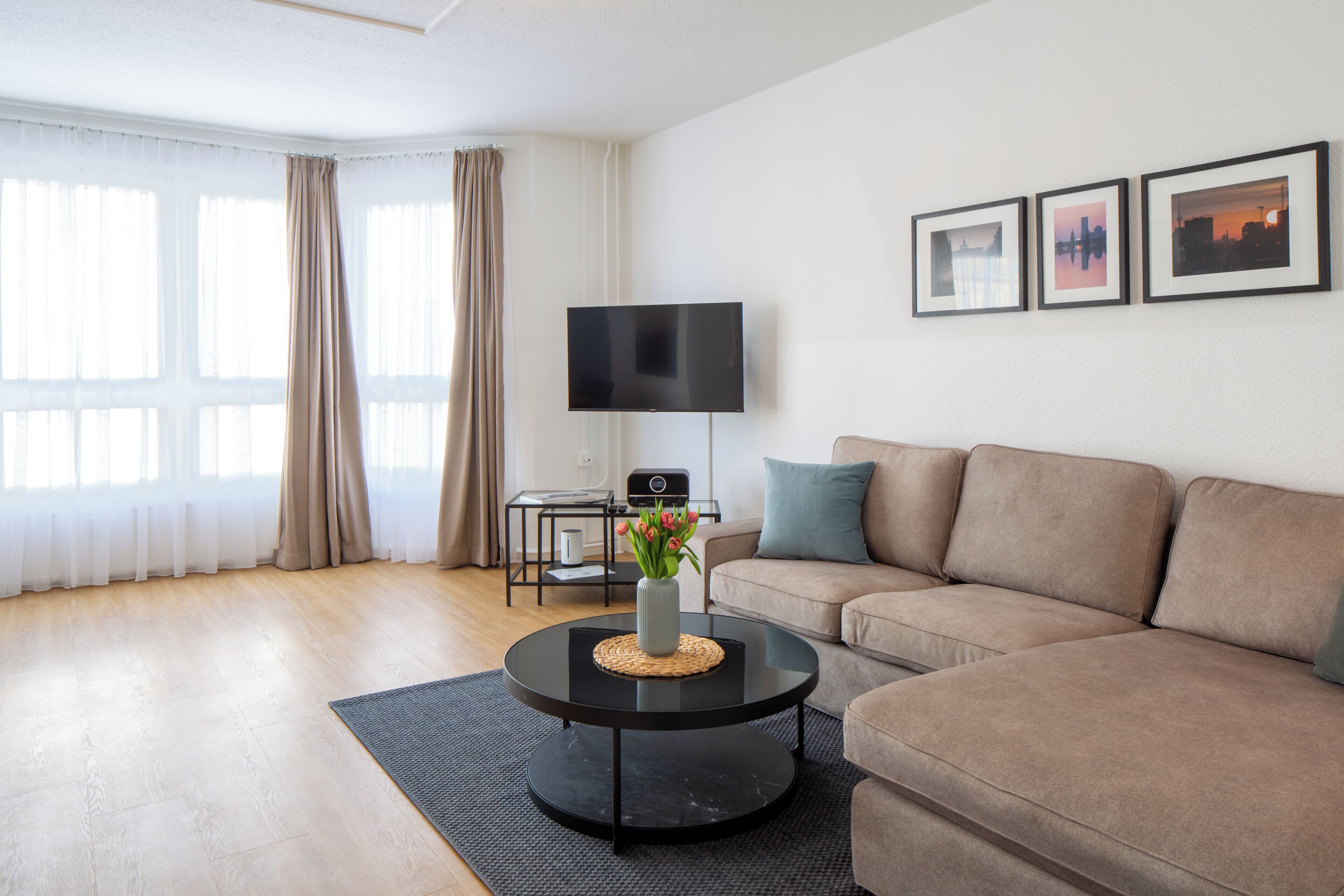 A living room with a sofa, a coffee table, a flat-screen TV, and a vase with flowers.