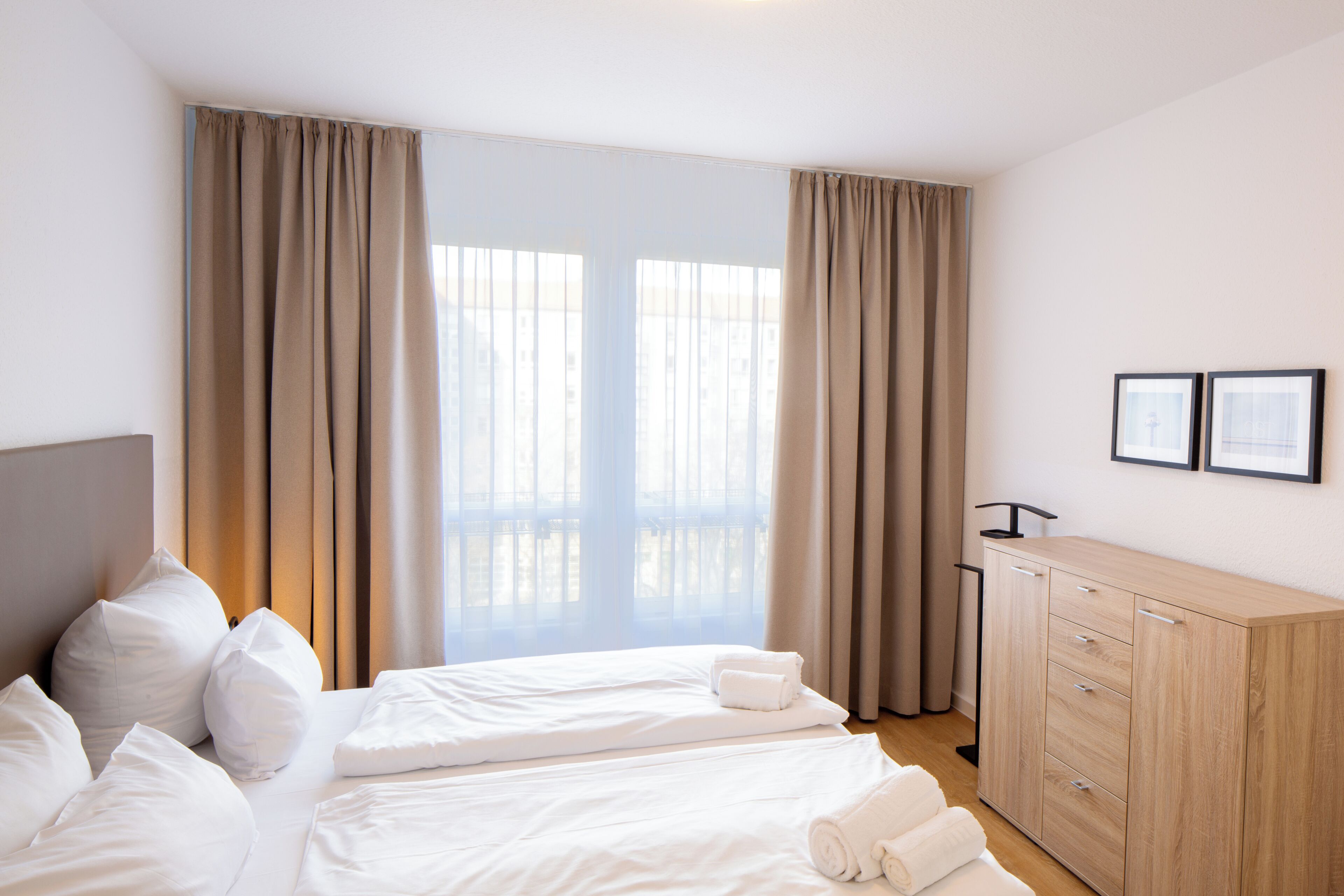 A hotel room with a bed, a wooden dresser, and a view through the window.