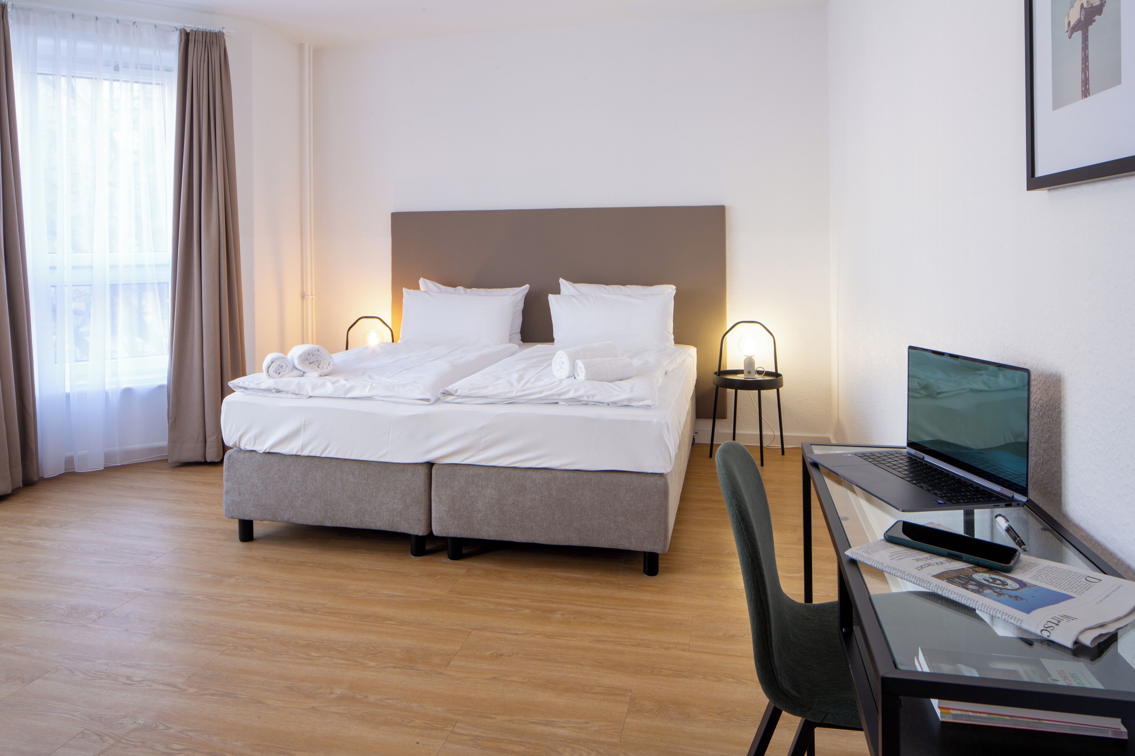 A hotel room with a bed, a desk with a laptop, and a chair.