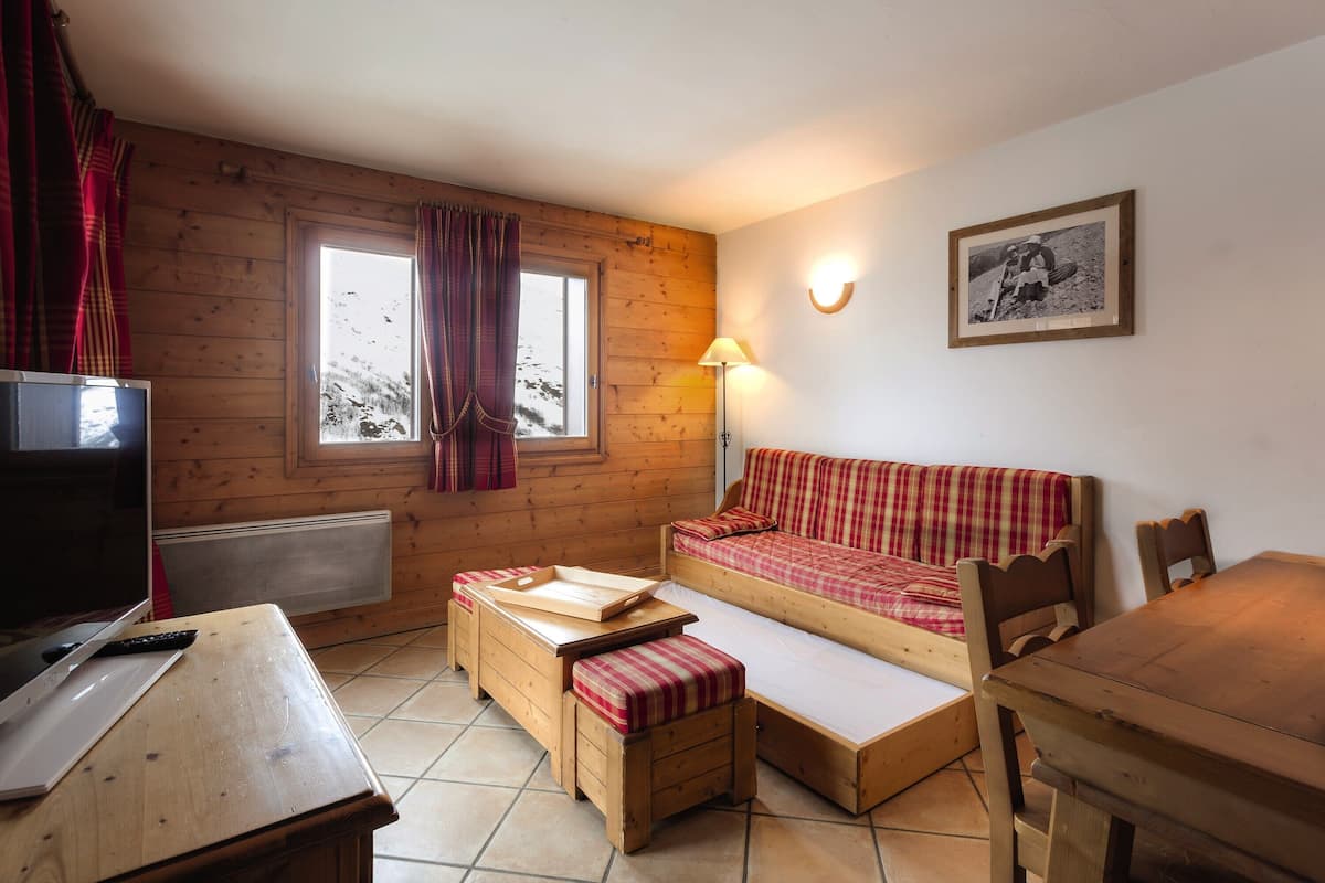 A cozy room with a wooden floor, a sofa bed, a small table, a TV, and a framed picture on the wall.