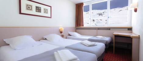 A hotel room with two beds, a desk, and a window with a mountain view.
