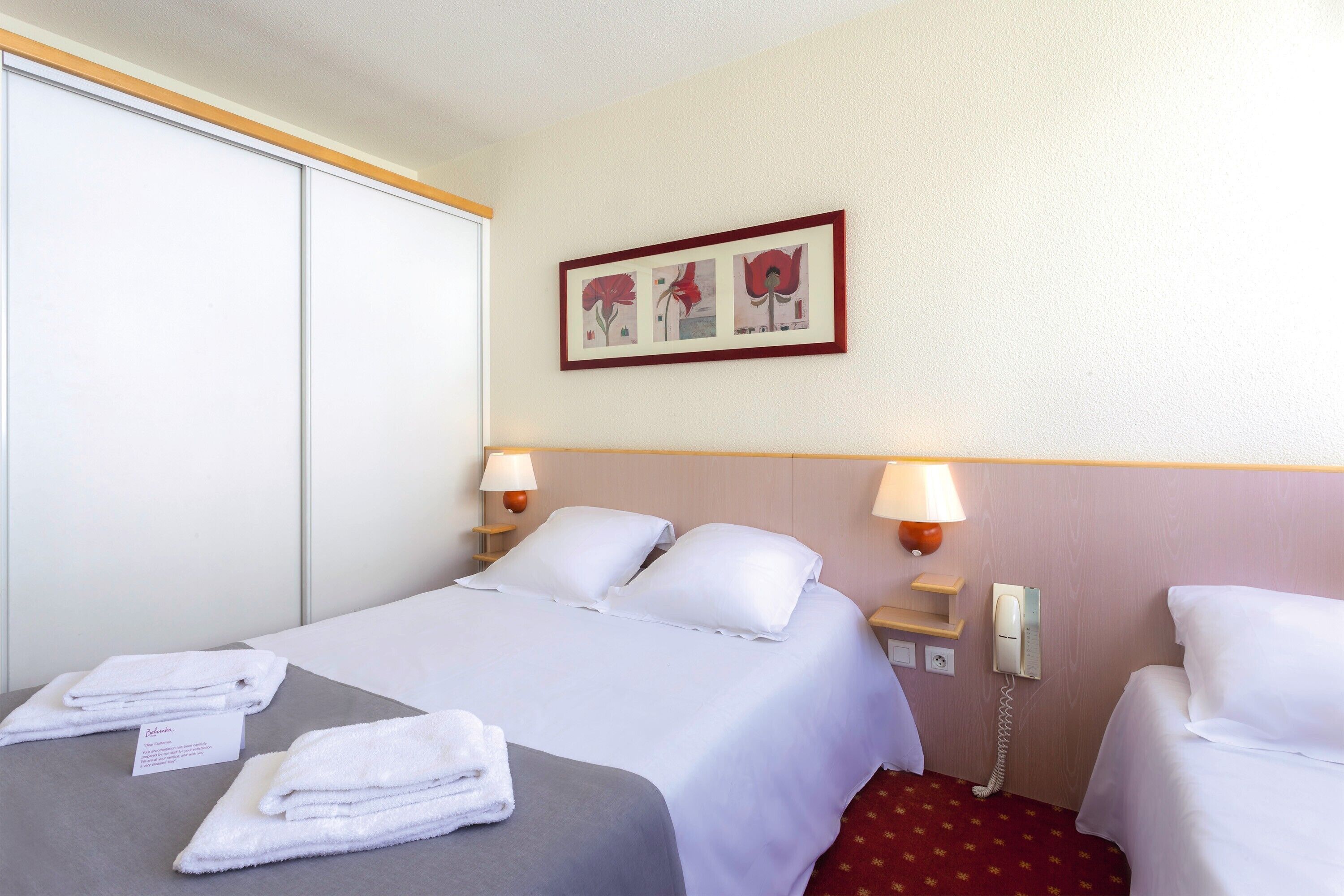 Een hotelkamer met een bed, twee bedlampen, een telefoon en een ingelijst schilderij aan de muur.
