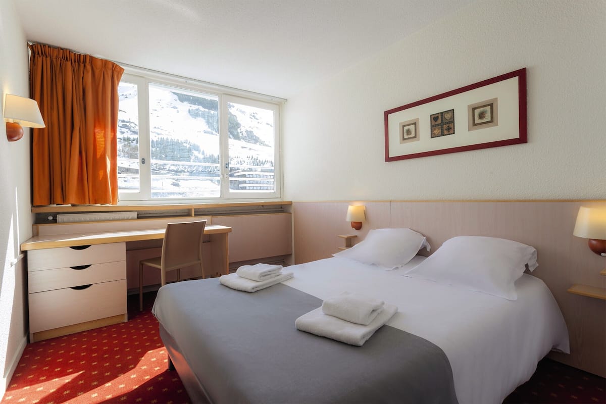 Ein Hotelzimmer mit Bett, Schreibtisch, Stuhl und einem Vorhangfenster.