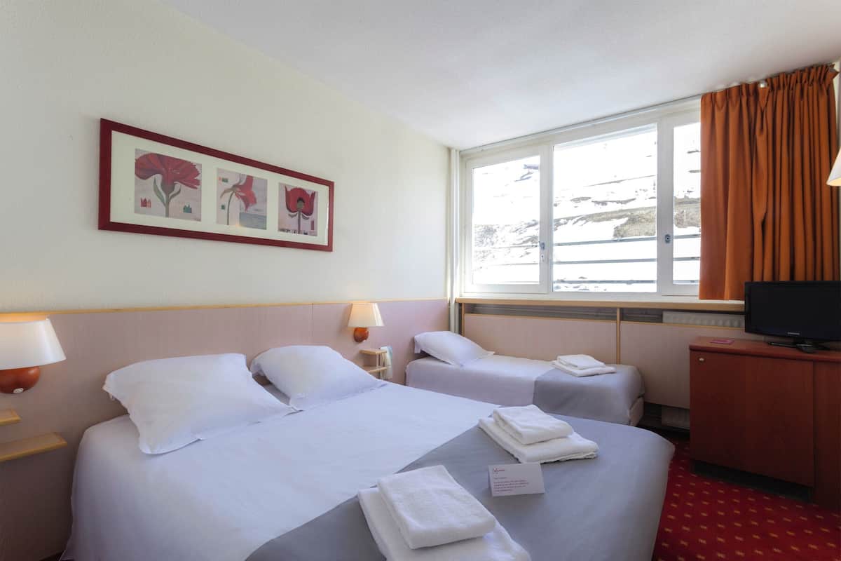 Ein Hotelzimmer mit zwei Betten, einem Fernseher und einem Fenster mit Vorhängen.