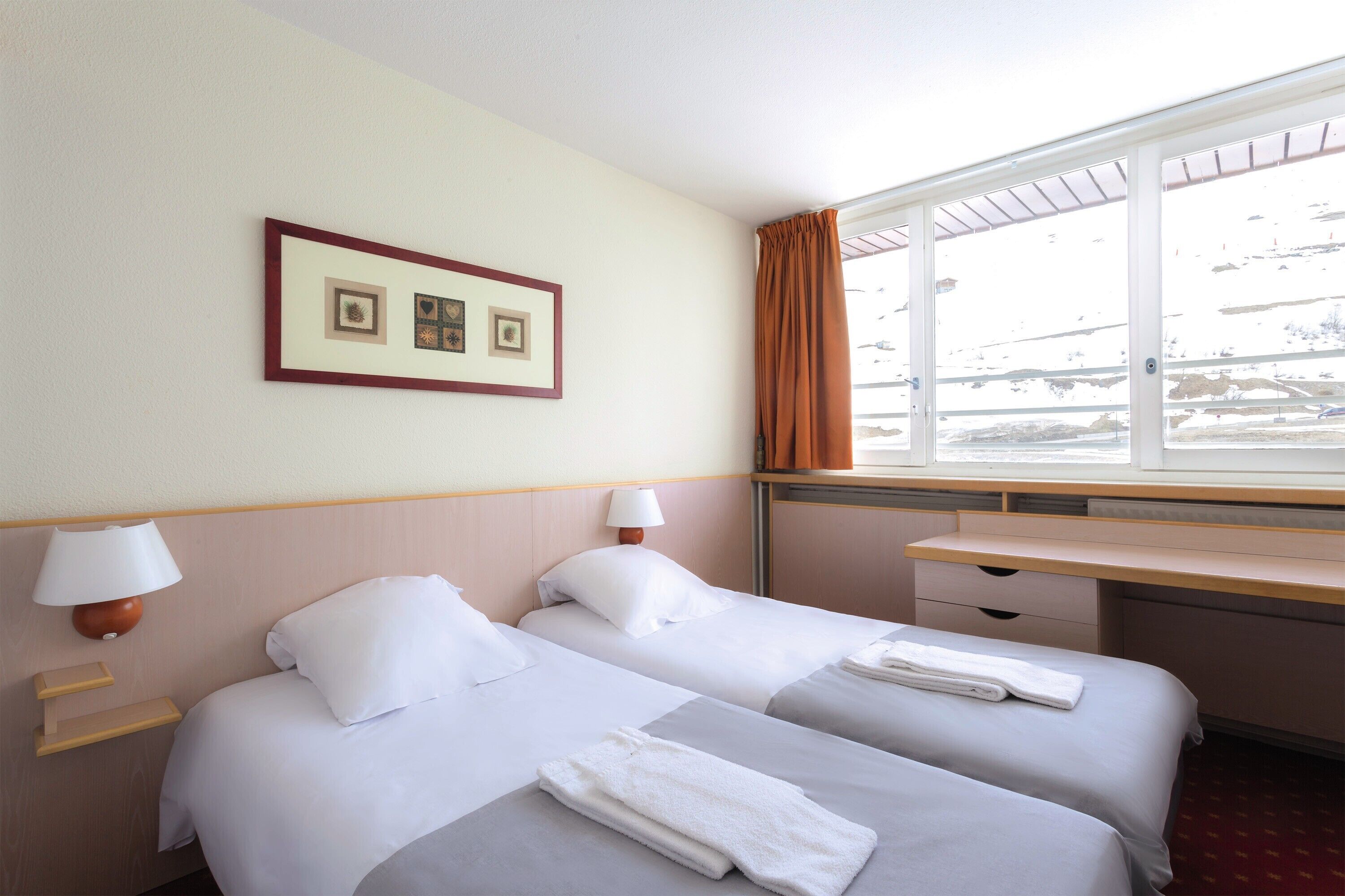 Une chambre d’hôtel avec deux lits, un bureau et une fenêtre avec des rideaux.