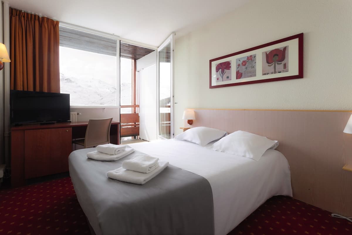 Ein Hotelzimmer mit einem Bett, einem Schreibtisch, einem Fernseher und einem Vorhangfenster.