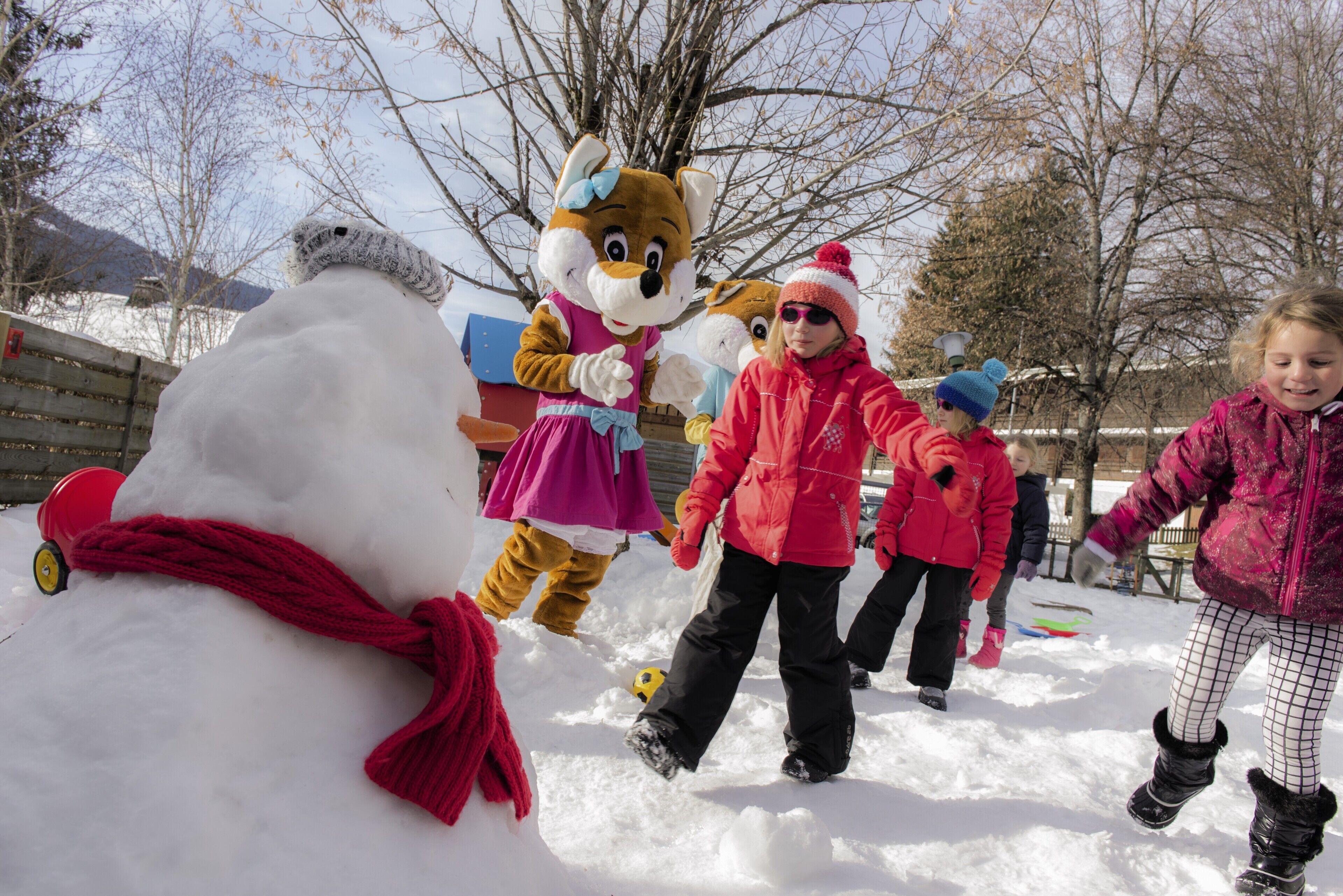 A snowman with a red scarf and a person in a red jacket standing next to it.