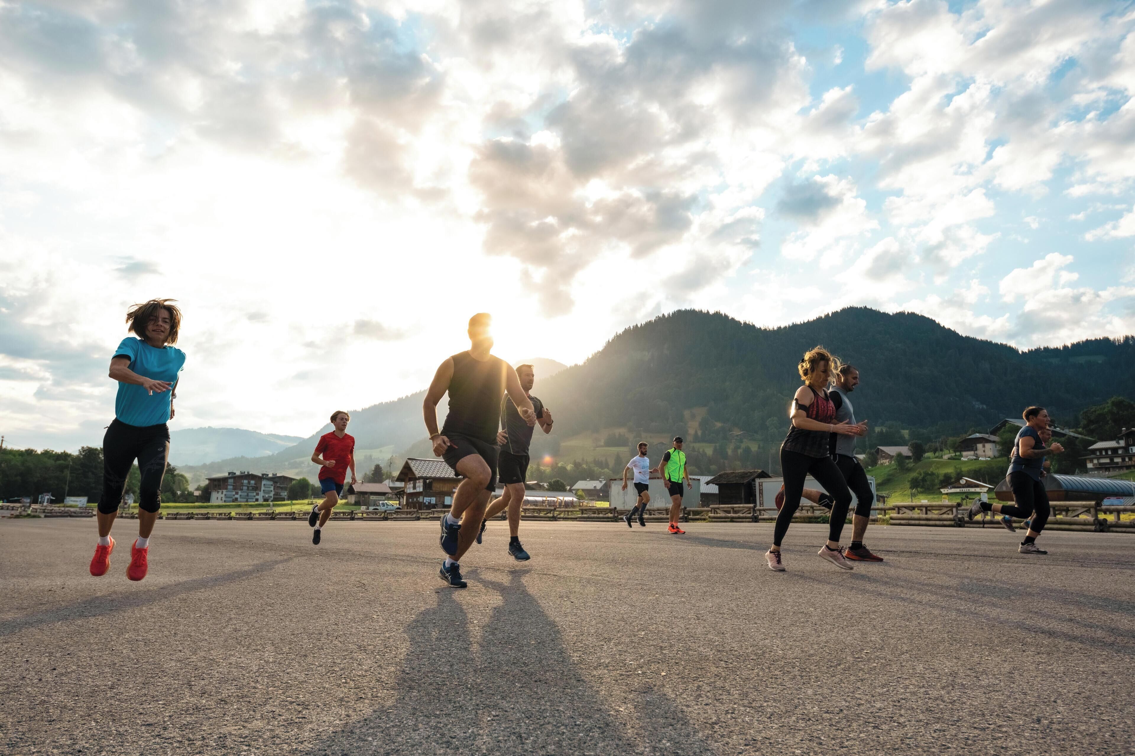 Eine Gruppe von Menschen joggt auf einem befestigten Weg vor einer Bergkulisse.