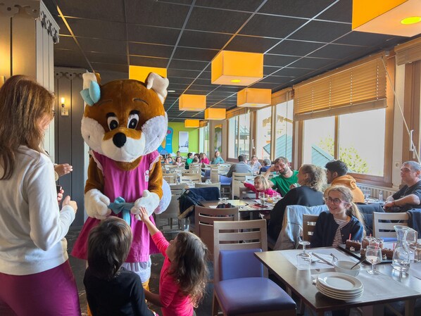 A restaurant with a mascot character, tables with diners, and a modern interior design.