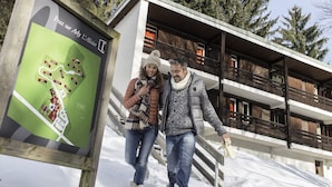 A wooden sign with a map and text, a modern building with balconies, and a snowy landscape. - Belambra Clubs Praz-sur-Arly - L'Alisier (Praz-sur-Arly)