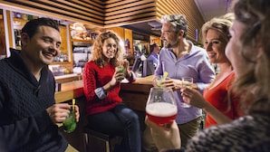 A group of people sitting at a bar with drinks, wooden paneling on the ceiling, and a bar counter with bottles and glasses. - Belambra Clubs Praz-sur-Arly - L'Alisier (Praz-sur-Arly)