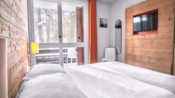 Une chambre à coucher avec un lit, une fenêtre avec des rideaux, une télévision et une chaise.