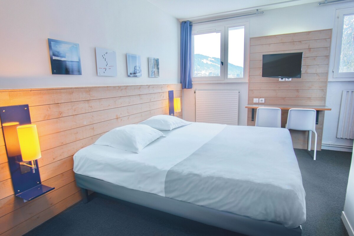 Une chambre d’hôtel équipée d’un lit, d’un bureau, d’une chaise, d’une télévision et d’œuvres d’art accrochées au mur.