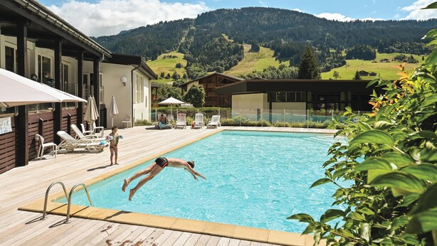 A swimming pool with a wooden deck, lounge chairs, and a view of a mountainous landscape. - Belambra Clubs Praz-sur-Arly - L'Alisier (Praz-sur-Arly)