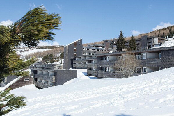 Un edificio moderno de varios pisos con techo inclinado, rodeado de suelo y árboles cubiertos de nieve.