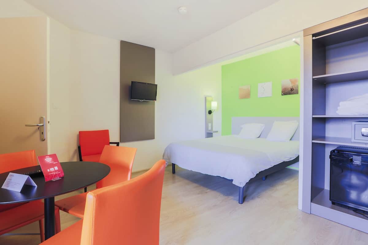 Une chambre d’hôtel comprenant un lit, un téléviseur fixé au mur, une table avec des chaises et une armoire.