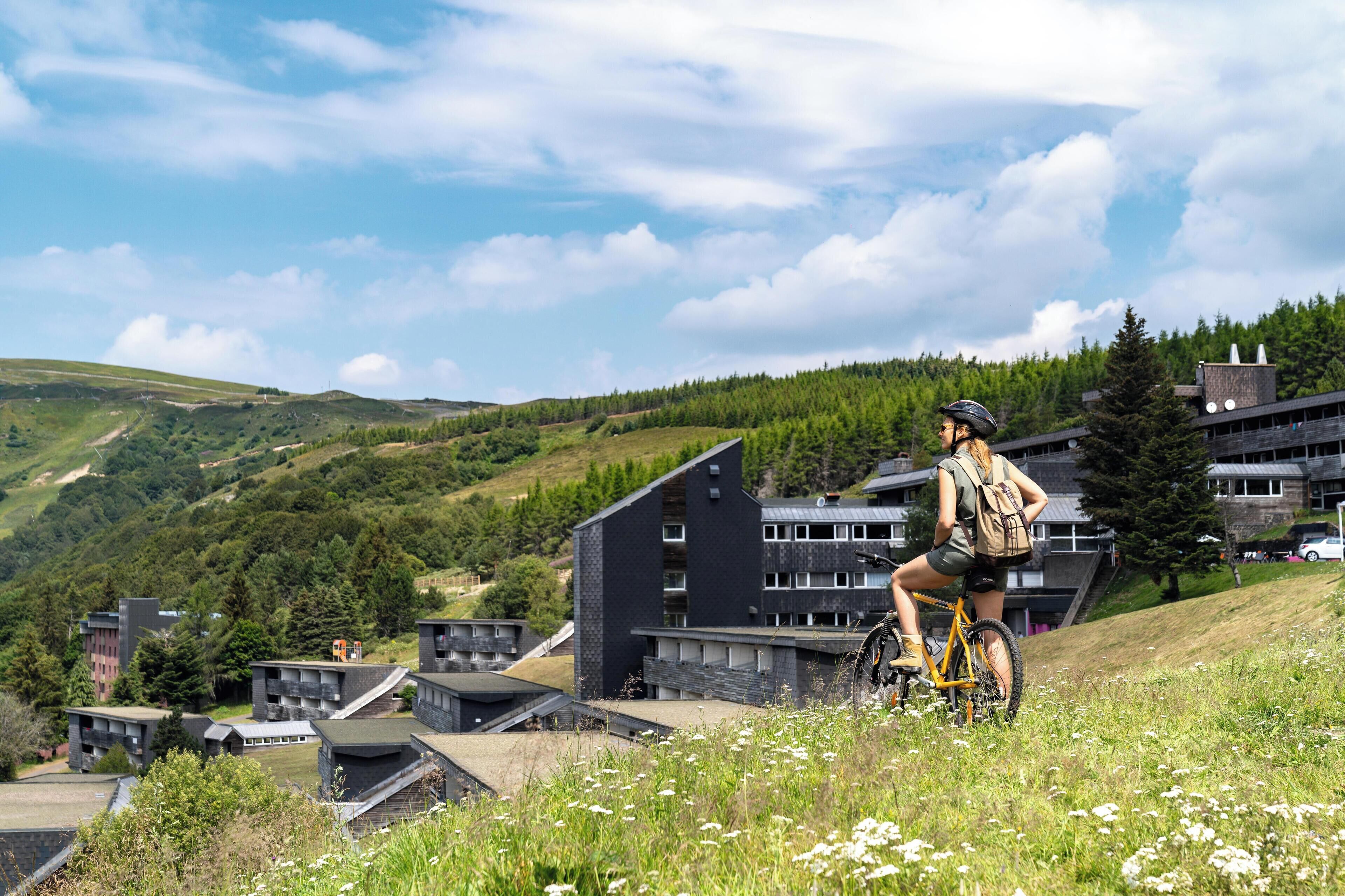 A person riding a bicycle on a grassy hill with modern buildings in the background.