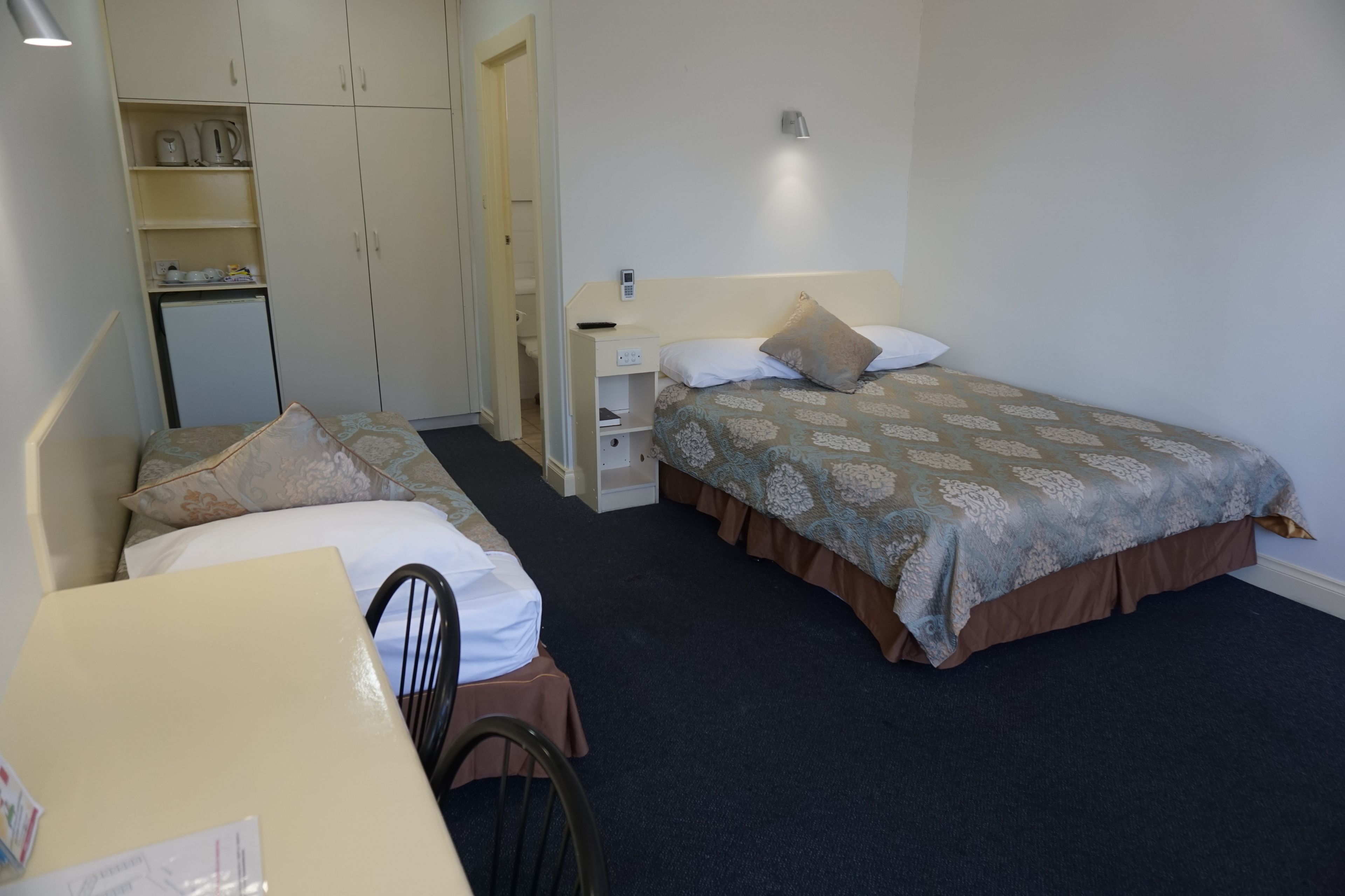 Una camera d'albergo con due letti, una scrivania, una sedia, un armadio e un angolo cottura.